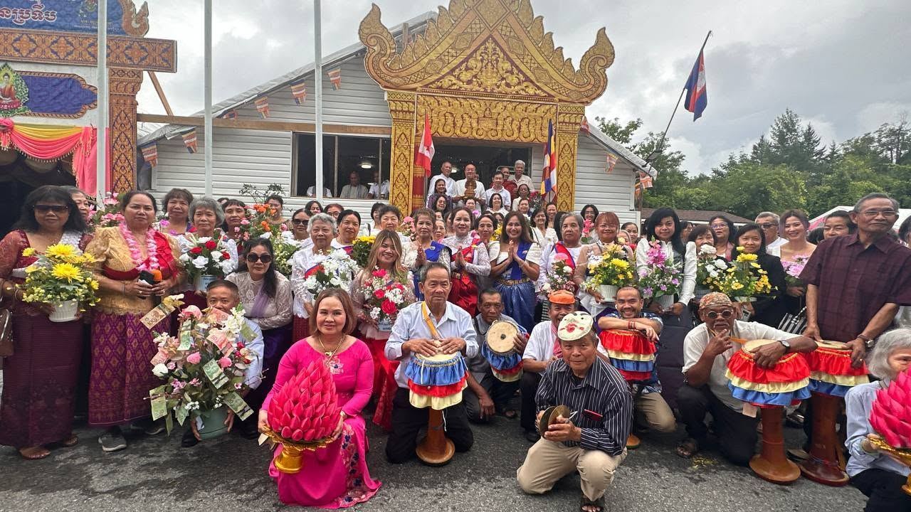 Families kneeling and standing with flower arrangements and drums at the temple gate