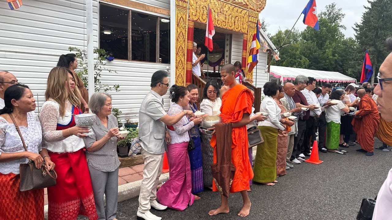 Community members lining up to offer food to a monk outside the temple