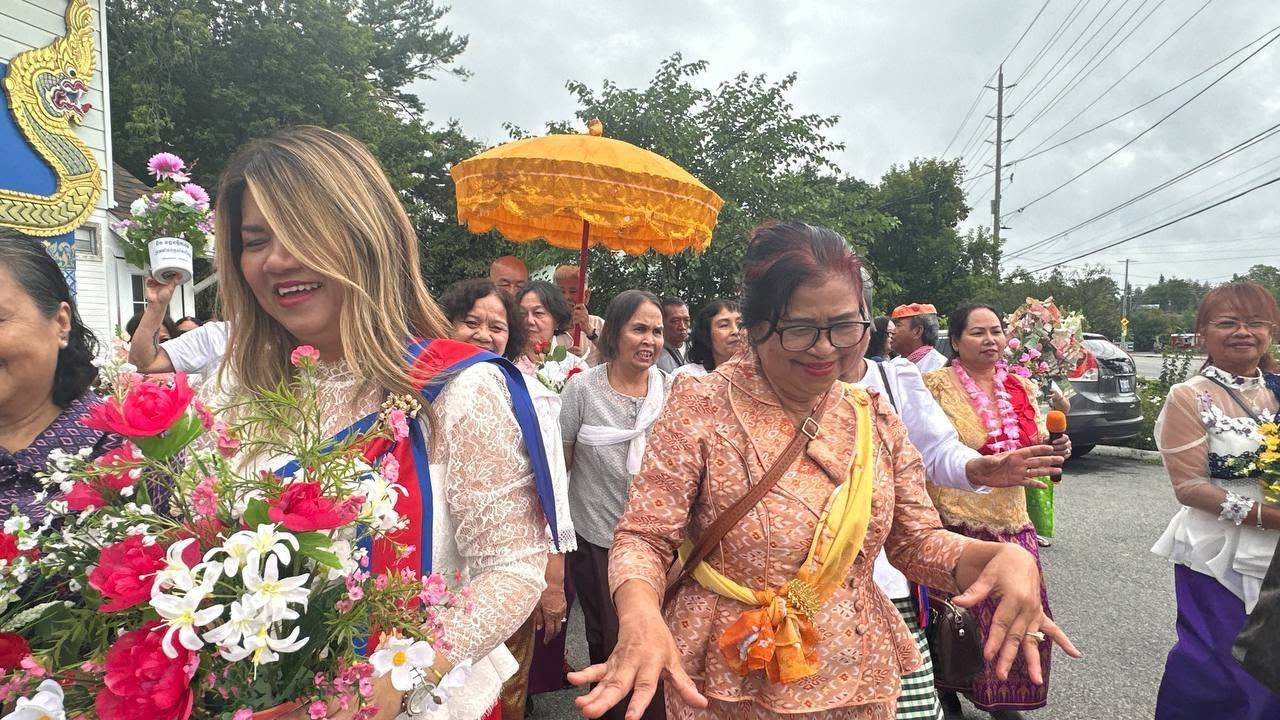 Women carrying bouquets of flowers in the procession, one smiling at the camera