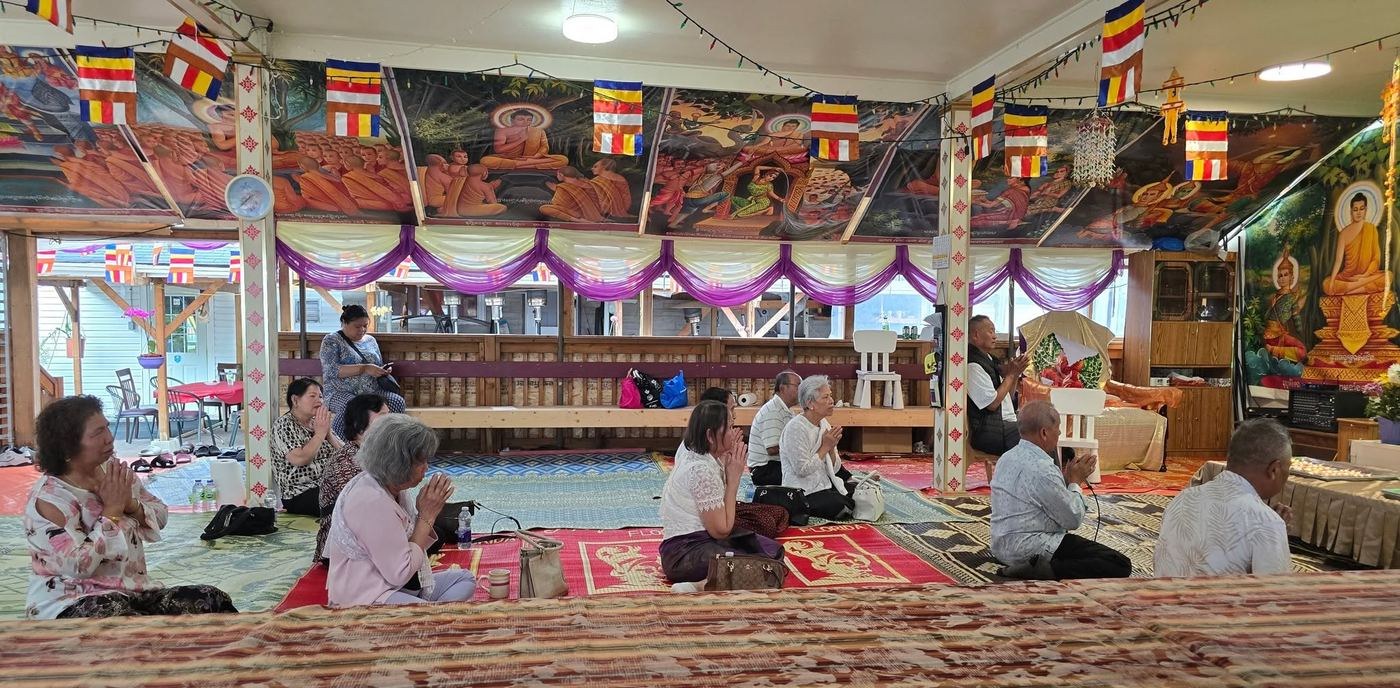 Elders praying on red carpets in the temple hall, under strings of Buddhist flags