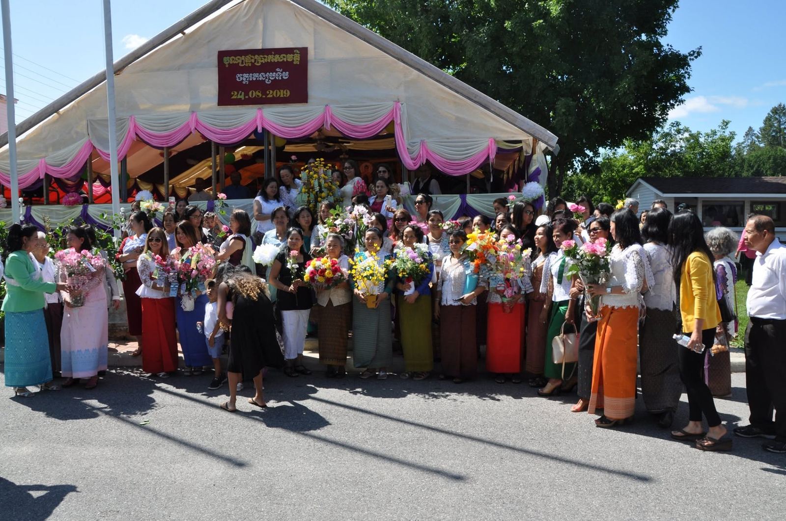 Community members holding bouquets of flowers in front of a white festival tent with pink drapes
