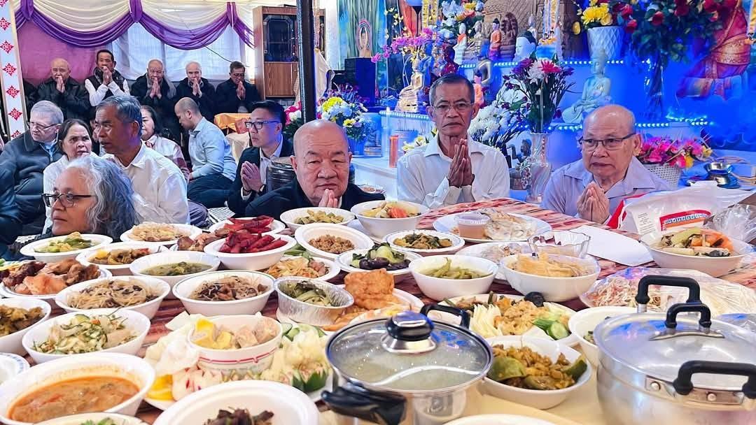 A table of home-cooked festival dishes, with elders praying behind it in front of the shrine