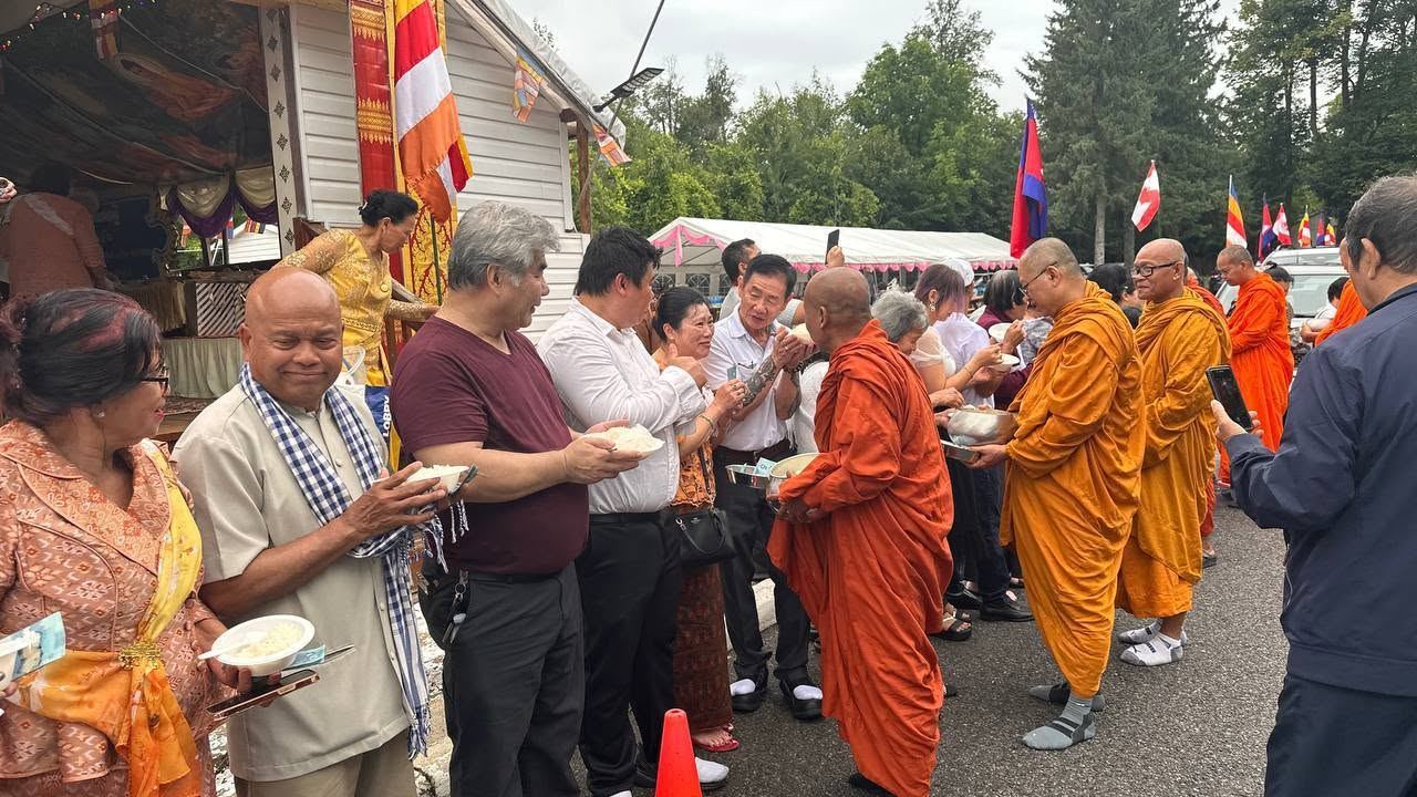 Community members offering food to monks in saffron robes outside the temple