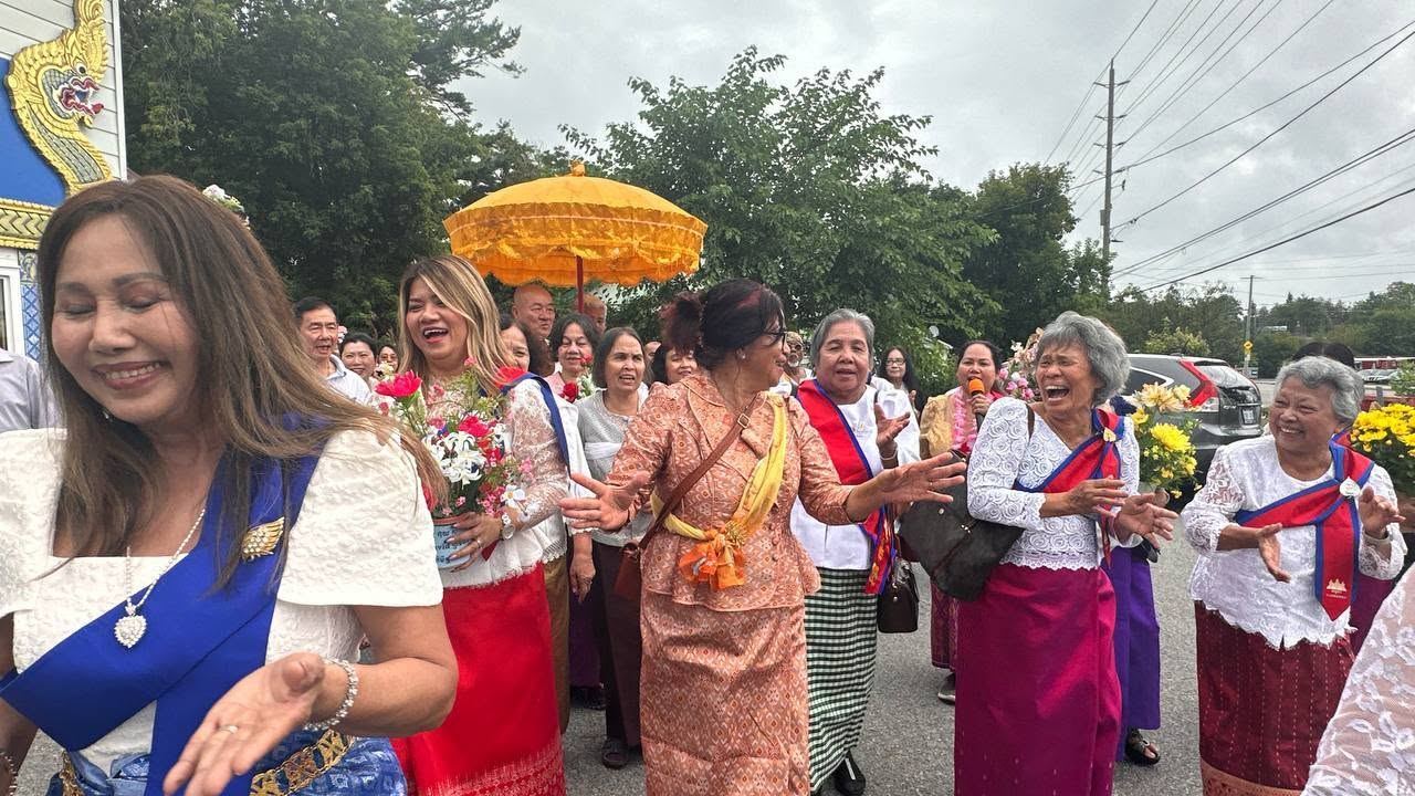A woman in a blue sash laughing as the procession passes, with a golden umbrella behind her